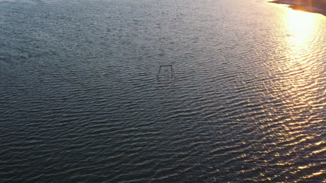 Picturesque-summertime-view-of-Salton-rippling-water-sea-with-abandoned-childhood-wooden-swing-set-in-ocean,-above-rising-circle-aerial