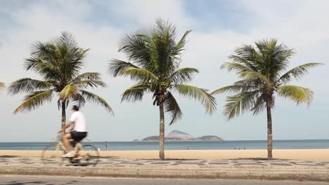 Personas-Con-Y-Sin-Máscaras-Faciales-Corriendo,-Trotando,-Andando-En-Bicicleta,-Caminando,-Andando-En-Bicicleta-Y-En-Patineta-Pasando-Tres-Palmeras-Y-La-Playa-De-Ipanema-Durante-El-Brote-De-Coronavirus-Covid-19