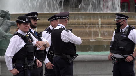 Vier-Polizisten-Beobachten-Die-Situation-Vor-Einem-Brunnen-Auf-Dem-Trafalgar-Square,-Während-Die-Öffentlichkeit-Vorbeigeht