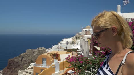 Hermosa-Mujer-Rubia-Haciendo-Turismo-En-Oia,-Santorini,-Grecia,-Tiro-Lateral