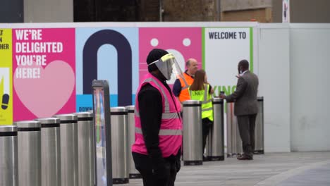 Man-wearing-protective-clothing-helps-train-passengers-at-Kings-Cross-Station,-London,-UK