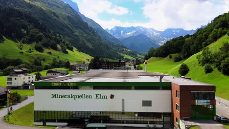 Lowering-aerial-cinematic-crane-shot-of-Elmer-mineral-water-plant-in-Elm,-Glarus,-Switzerland