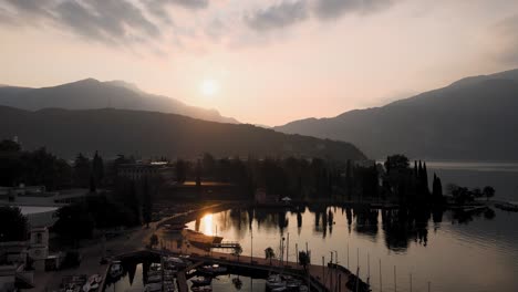 Luftaufnahme-Des-Sonnenaufgangs-über-Dem-Gardasee-Und-Dem-Stadthafen-Von-Riva-Del-Garda,-Italien