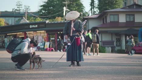 Enfoque-Turístico-Y-Acarició-Al-Lindo-Perro-Samurai-De-Pie-Junto-Al-Samurai-Japonés-Flautista-Tocando-Shakuhachi-En-El-Parque-Maruyama,-Kyoto,-Japón