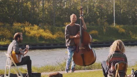 Musicians-playing-outside-on-a-sunny-day-on-river-bank,-zoom-out-slowmo