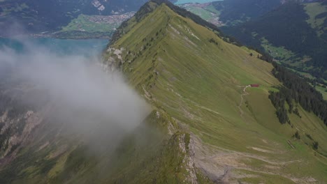 Drone-shot-flying-over-the-ridge-of-Morgenberghorn-with-its-steep-slopes-on-both-sides-with-a-small-thin-cloud-flying-by
