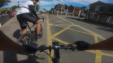 POV-View-Of-Cyclists-Waiting-By-Box-Junction-By-Traffic-Lights-Beside-Bushey-Railway-Station