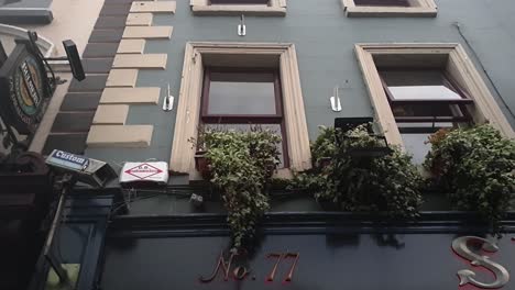 Tilting-down-shot-of-a-closed-pub-in-Dublin-because-of-COVID-with-people-walking-by,-bars-will-have-issues-with-opening-because-of-social-distancing