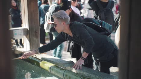 Tourists-Drinking-And-Washing-Hands-Using-Wooden-Ladles-At-The-Temizuya-Before-Entering-The-Hirano-Jinja-Shrine-In-Kyoto,-Japan