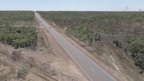 Slow-moving-drone-shot-of-car,-4WD-driving-down-a-long-straight-Highway-in-Northern-Territory,-Australian-Outback