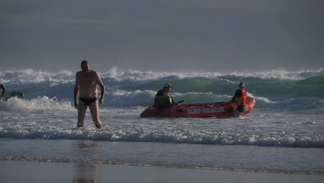 Hombre-Saliendo-Del-Océano-Después-De-Disfrutar-Nadando-En-Verano---Equipo-Salvavidas-De-Surf-En-Servicio-En-Un-Bote-De-Rescate---Playa-Currumbin-En-Gold-Coast,-Qld,-Australia