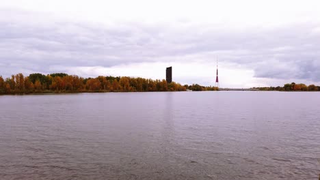 Television-tower-of-Riga-from-Dauguva-river-shore-with-calm-and-still-water-in-cloudy-autumn-day