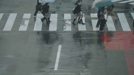 Menschen-Und-Studenten,-Die-An-Einem-Regnerischen-Tag-Mit-Reflexion-Auf-Nasser-Straße-In-Shibuya-Crossing,-Tokio,-Japan,-Hinübergehen