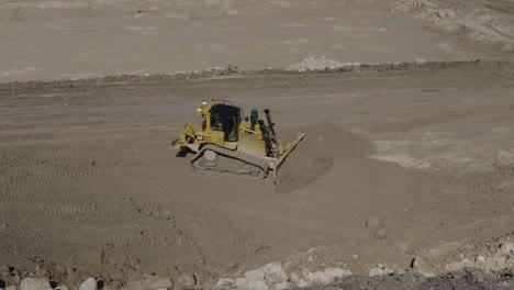 Toma-Aérea-En-Círculos-De-Una-Excavadora-John-Deere-450d-Cargando-Tierra-En-Un-Camión-De-Roca-En-Un-Sitio-De-Construcción