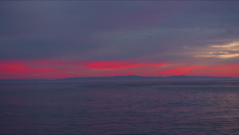 Seevögel-Fliegen-Durch-Den-Himmel-Mit-Wunderschönem-Rosa-Und-Orangefarbenen-Sonnenuntergang-Und-Blicken-Mit-Segelbooten-Auf-Das-Meer