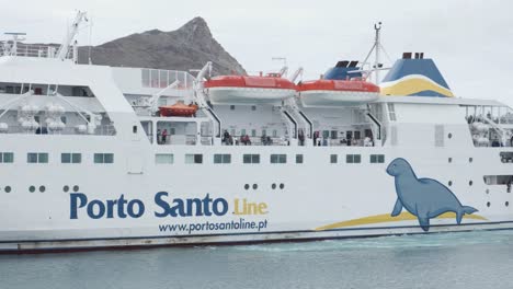White-passenger-Porto-Santo-boat-docked-at-port-pier-in-harbor,-Portugal,-handheld-close-up-profile-pan-right