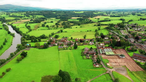 Aerial-forward-motion-shot-of-a-rural-town-in-England-with-a-steam-train-passing,-green-landscape