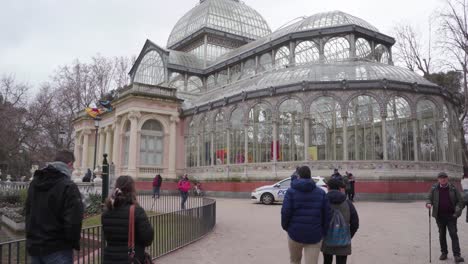 Tourists-Strolling-Around-With-A-Police-Car-Parked-Outside-The-Iconic-Palacio-De-Cristal-At-The-Retiro-Park-In-Madrid,-Spain---wide-shot
