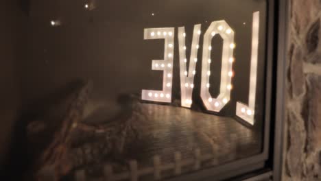 Reflection-off-the-glass-of-a-fire-place-at-a-wedding-reception-of-a-giant-lit-up-Love-letter-sign