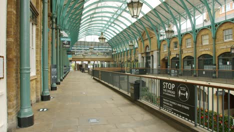 Lockdown-in-London,-one-lone-person-walks-through-deserted-Covent-Garden-Piazza-with-Coronavirus-signage,-during-the-2020-pandemic