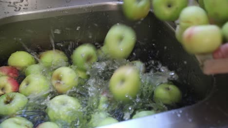 Frau-Gießt-Grüne-Äpfel-Auf-Die-Mit-Wasser-Gefüllte-Küchenspüle-–-Handheld,-Nahaufnahme