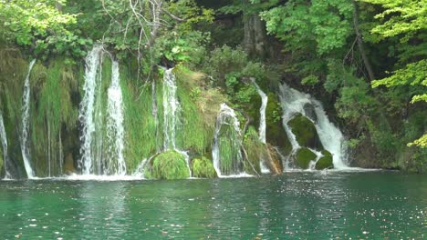 A-series-of-waterfalls-flowing-through-grass-and-mossy-rocks-into-a-turquoise-pool-at-Plitvice-Lakes-National-Park-in-Croatia,-Europe-at-¼-speed