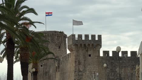 Tower-Kamerlengo-at-the-end-of-the-row-of-palm-trees-in-the-town-of-Trogir-in-Croatia-with-the-country-and-city-flags-blowing