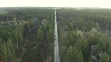 Following-a-car-in-front-view-from-a-drone-flying-in-it's-driving-direction-over-a-autumn-colored-forest