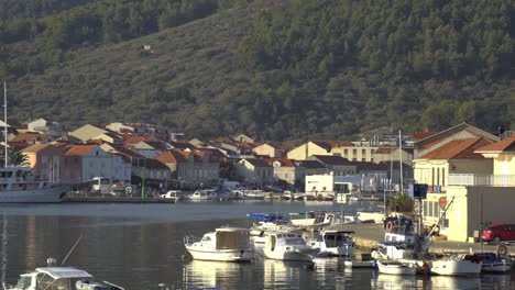 Barcos-Atracados-En-Vela-Luka,-Croacia,-Con-Edificios-Que-Bordean-El-Agua-Y-Colinas-En-El-Fondo