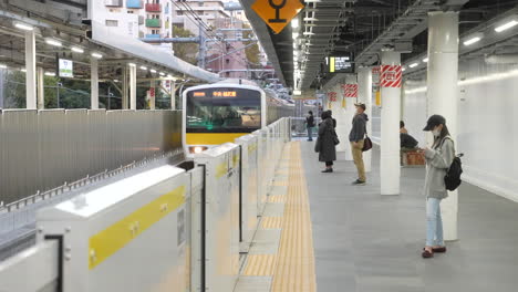 Lugareños-Japoneses-Con-Mascarilla-En-La-Plataforma-Con-El-Tren-Que-Se-Acerca-A-La-Estación-De-Metro-Durante-El-Día-En-Tokio,-Japón