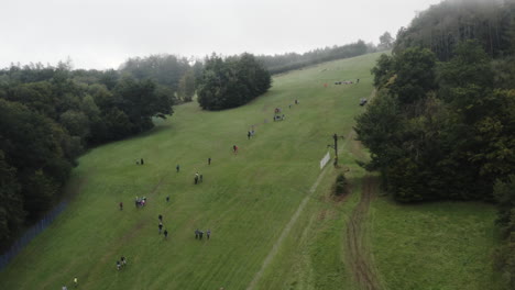Aerial-Shot-Of-Crowds-Of-People-On-A-Mountain-Watching-A-Downhill-Grass-Ski-Competition,-Extreme-Sport