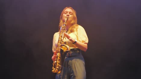 Mujer-Joven-Tocando-Música-En-El-Saxofón-Bajo-Las-Luces-Del-Escenario