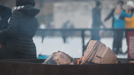 Handheld-shot-of-outdoor-fire-pit-with-ice-skaters-in-background