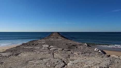 Pov-walk-on-emtpy-beach-along-endless-old-stone-jetty-in-front-of-the-sea