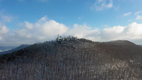 Aerial-flying-away-from-medieval-Castle-Teck-on-a-mountain-on-a-snowy-day-during-winter-in-Swabia,-Germany