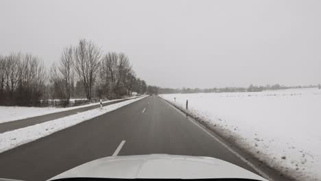 Conduciendo-A-Través-De-Un-Paisaje-Invernal-En-Coche-En-Un-Ambiente-Rural-Mientras-Cae-Algo-De-Nieve