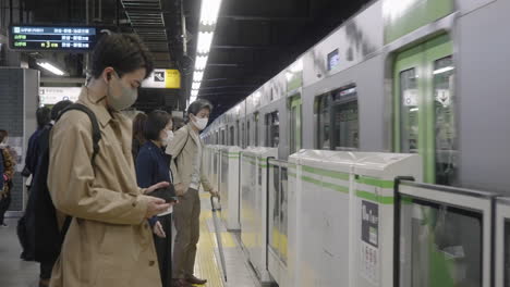U-Bahn-Plattform-Mit-Passagieren-In-Gesichtsmaske,-Die-Stehen,-Während-Sich-Der-Zug-Auf-Der-Yamanote-Linie,-Tokio,-Japan,-Nähert