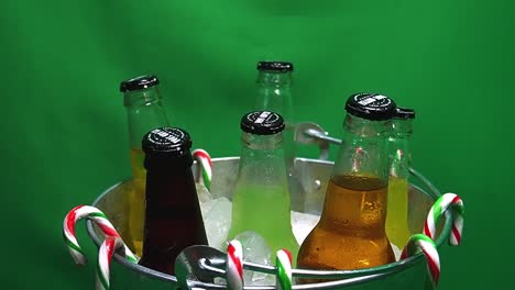 2-3-Schleifen-Grüner-Bildschirm,-Rotierender-Metallischer-Partyeimer-Mit-Kohlensäurehaltigen-Insel-Sodagetränken-In-Eis-Mit-Hängenden-Zuckerstangen-Und-Wassertropfen-Auf-Glasflaschen-Mit-Mango,-Ingwer,-Kiefer,-Apfel,-Limette,-Cola-Creme