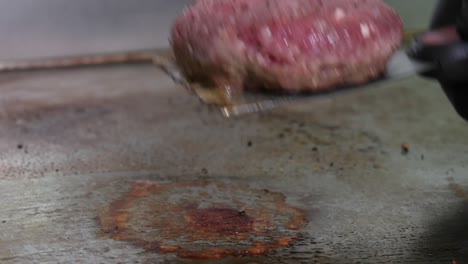 Close-up-of-a-hamburger-patty-being-flipped-on-a-restaurant-griddle-while-cooking