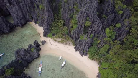 Aerial-pedestal-down-on-beach-by-limestone-cliffs-at-Secret-Lagoon-in-El-Nido,-Palawan,-the-Philippines-slightly-pan-left