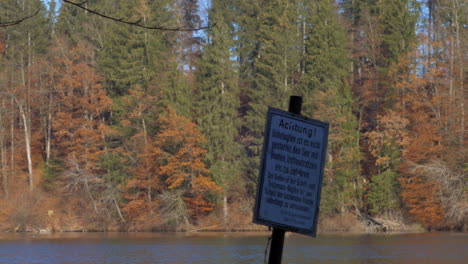 Pan-shot-of-a-lake-in-late-autumn,-with-a-sign-in-the-foreground,-prohibiting-boats-and-inflatables,-at-Hackensee-near-Holzkirchen