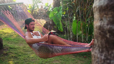 A-caucasian-man-takes-a-rest-from-his-travels-by-reading-a-book-in-a-hammock-in-Punta-Banco,-Costa-Rica