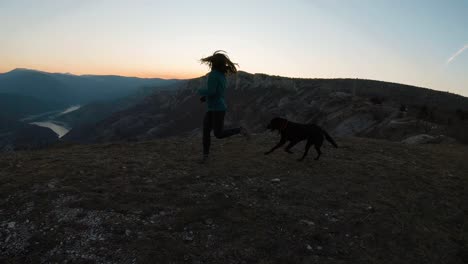 Young-girl-running-with-a-black-labradot-dog-on-a-mountain