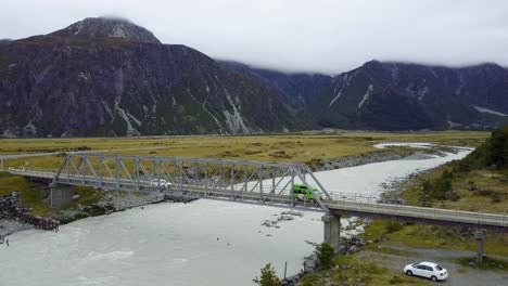 A-drone-shot-of-a-bridge-over-a-river-in-the-mountains,-with-cars-driving-pass-by-the-bridge-in-Mt
