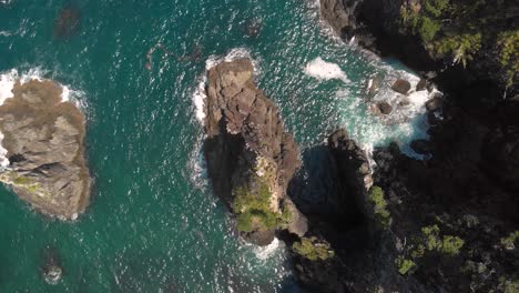 Aerial-drone-topdown-view-flying-over-big-sharp-rocks-near-a-paradise-coast