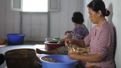 Group-of-local-women-sitting-on-floor,-working-in-a-crisp-factory-filling-bags-from-filled-buckets-in-Indonesia,-Java