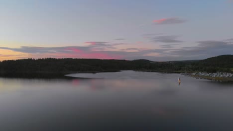 an-aerial-shot-over-a-calm-lake-at-beautiful-pink-sunset,-with-a-sailboat-in-sight,-short-version