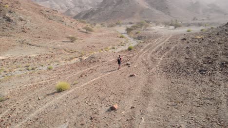 Aerial-circular-shot-from-drone-of-an-young-male-walking-in-a-rocky-desert-valleys-in-Hatta,-United-Arab-Emirates