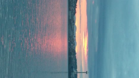 Seattle-City-Skyline-seen-from-the-bremeton-ferry-at-sunrise,-calm-waters-of-puget-sound,-mostly-overcast-clouds,-sunrise-reflecting-in-the-water,-vertical-orientation