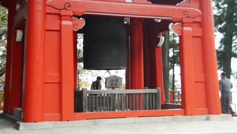 Japanese-woman-using-a-bell-in-a-red-shrine-on-mount-Hiei-zan,-Kyoto,-Japan